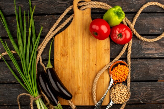 Овощи - вид сверху спелых овощей, таких как красные помидоры, баклажаны и зеленый болгарский перец вместе с фасолью и зеленью на деревенском деревянном столе