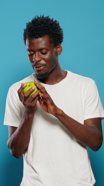 Vegetarian man playing with green apple in studio. Joyful person throwing fruits, feeling excited about healthy diet and nutrition. Adult looking at camera and presenting snack with vitamins