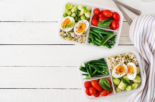 Vegetarian meal prep containers with eggs, brussel sprouts, green beans and tomato. Dinner in lunch box. Top view. Flat lay