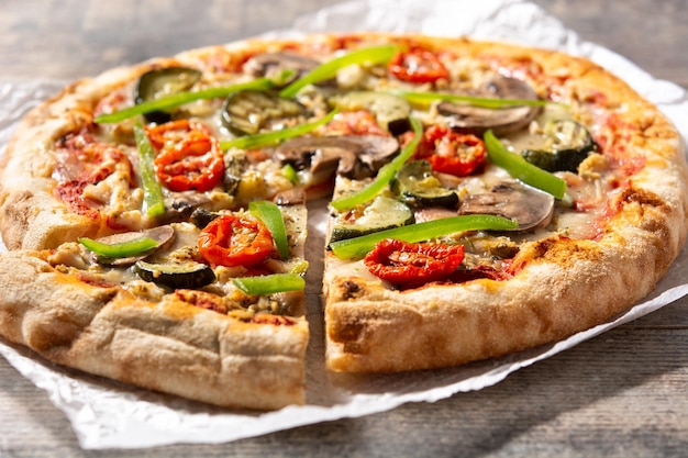 Vegetarian pizza with zucchini tomato peppers and mushrooms on wooden table