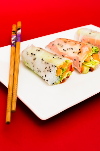 Free photo vegetarian rice paper rolls stuffed with vegetables on plate with wooden chopsticks