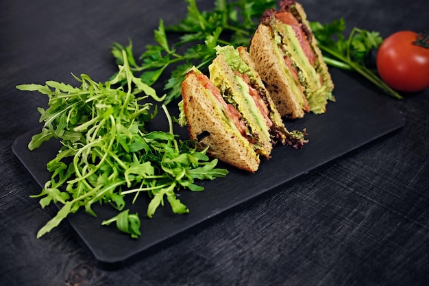 Vegetarian sandwich with salad and tomatoes on a wooden table surface.