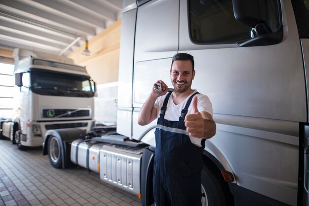 Vehicle mechanic with wrench tool and thumbs up standing in front of trucks in workshop