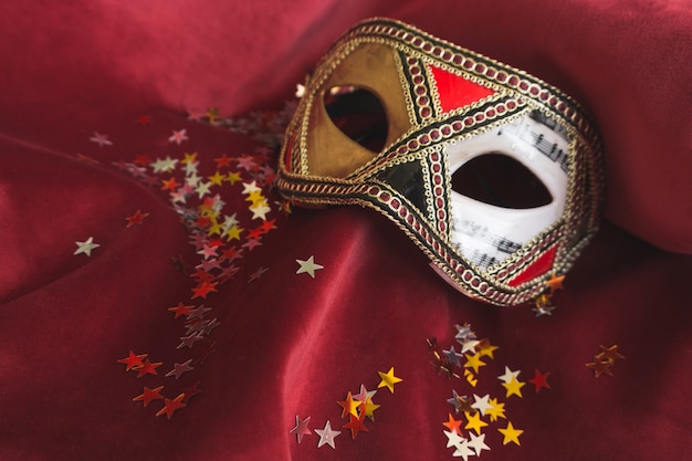 Бесплатное фото Венецианские маски на красной ткани с конфетти звезды
