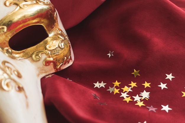 Venetian mask with a large nose on a red fabric with star confetti close up