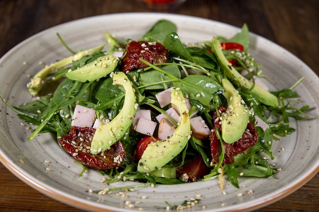 Οverhead shot of salad with tomatoes, sun-dried tomatoes, avocado, spinach, turkey and sesame top