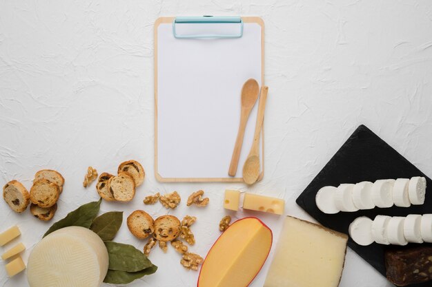 Verity of cheese; bread slice; walnut; bay leaves with empty clipboard