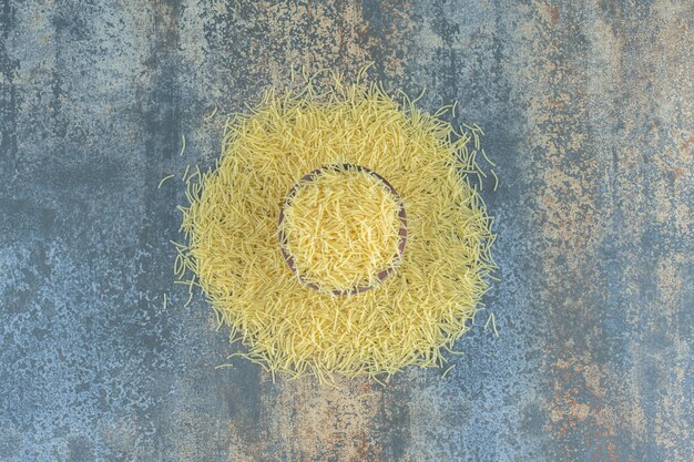 Vermicelli pasta scattered from a full bowl , on the marble surface.