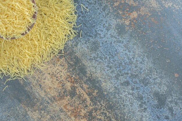 Vermicelli pasta scattered from a full bowl , on the marble surface.