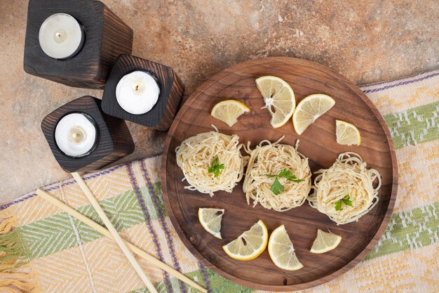 Vermicelli with lemon slices on wooden plate and candles.