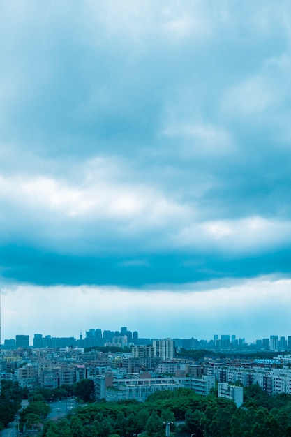 Vertical aerial shot of high city buildings under a cloudy light blue sky