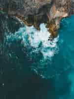 Free photo vertical aerial shot of sea waves hitting the cliff