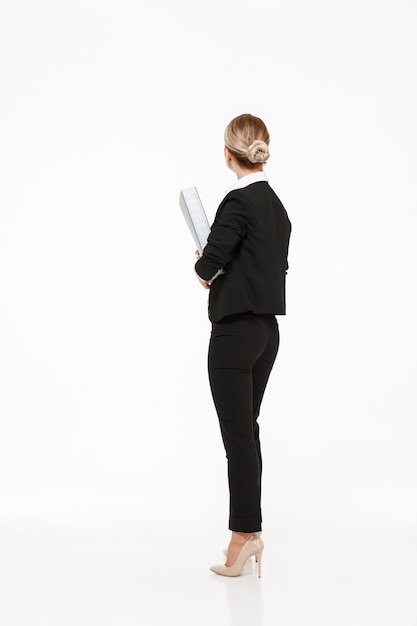 Vertical back view of blonde business woman holding big folder over white wall