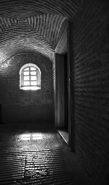 Vertical black and white shot of the inside of a building with a window during daytime