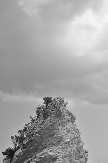 Vertical black and white shot of a rocky formation with clouds