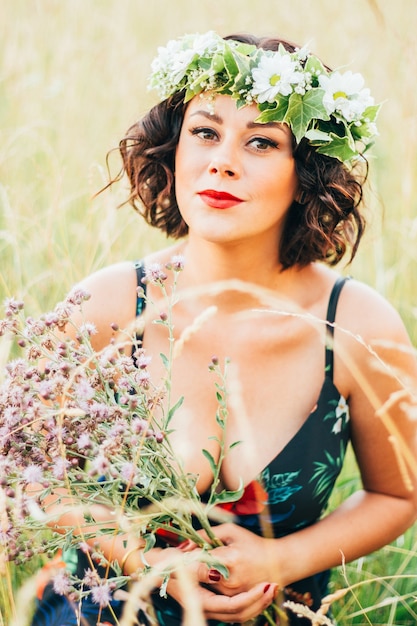 Foto gratuita verticale della donna caucasica con una corona di fiori che raccolgono fiori nel campo