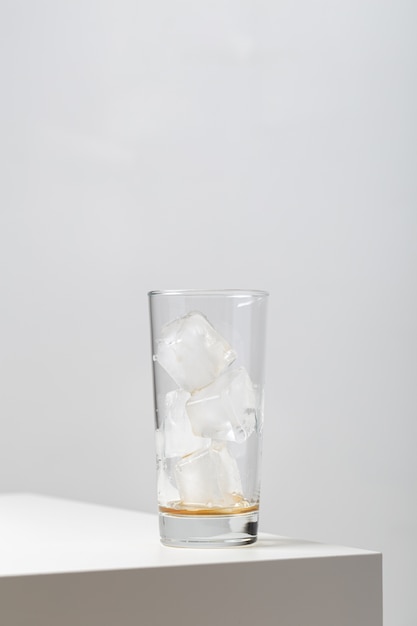 Вертикальный крупный план пустого стакана с кубиками льда в нем на столе под огнями