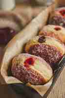 Free photo vertical closeup of fluffy doughnuts filled with jam in a container under the lights