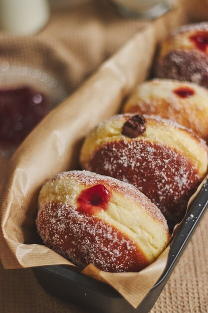 Vertical closeup of fluffy doughnuts filled with jam in a container under the lights