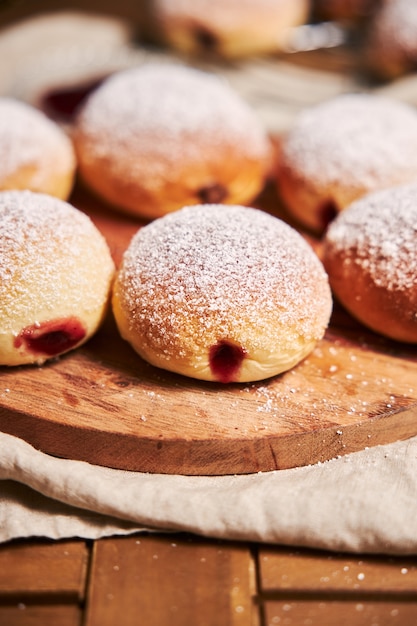 Vertical closeup of fluffy doughnuts filled with jam on a tray under the lights