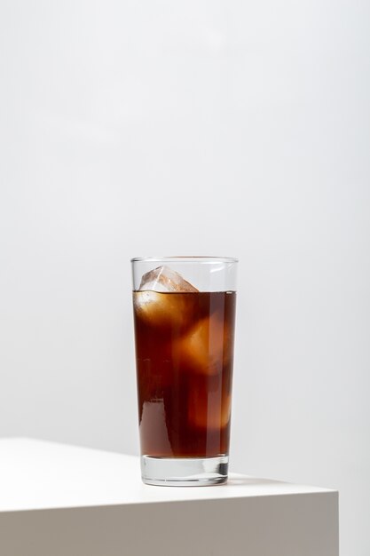 Vertical closeup of a glass of ice tea on the table under the lights against a white background