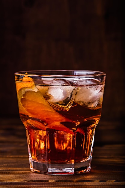 Vertical closeup of a homemade Negroni cocktail with ice and a slice of orange on a wooden table