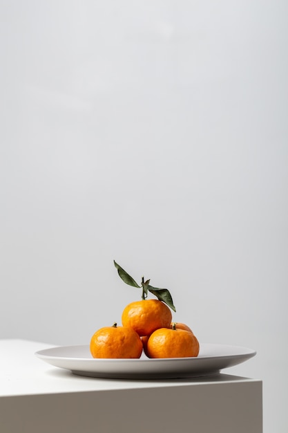 Vertical closeup of mandarines on a plate on the table under the lights against a white background