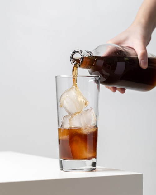 Vertical closeup of a person pouring tea in a glass with ice cubes in it on the table