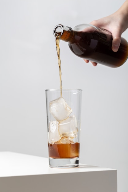 Free photo vertical closeup of a person pouring tea in a glass with ice cubes in it on the table