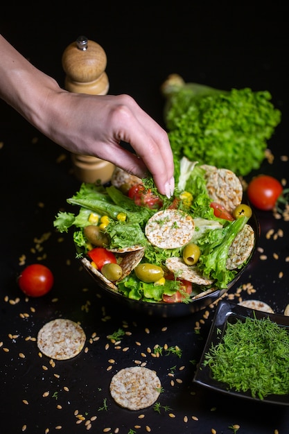 Free photo vertical closeup of a person putting herbs on salad in a bowl on the table under the lights