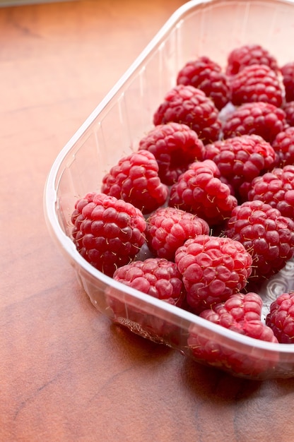 Vertical closeup of raspberries in a plastic container on the table under the lights
