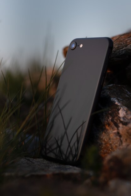Vertical closeup shot of a black smartphone leaned on a  stone