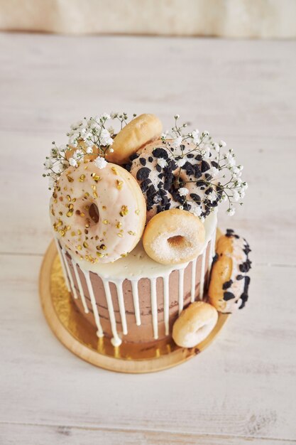 상단 및 흰색 물방울에 도넛이 있는 맛있는 도넛 초코 생일 케이크의 수직 근접 촬영