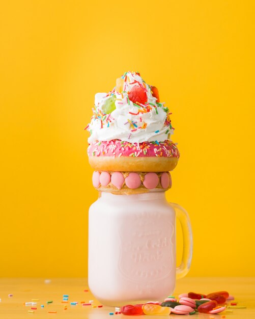 Vertical closeup shot of a dessert with a doughnut and whipped cream on a drinking jar