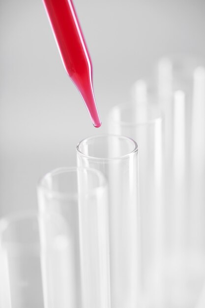 실험실에서 깨끗한 시험관 위에 붉은 액체가 있는 점적기의 수직 근접 촬영