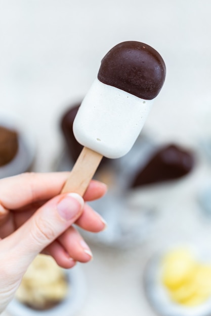 Vertical closeup shot of a female hand holding a raw vegan ice-cream on stick