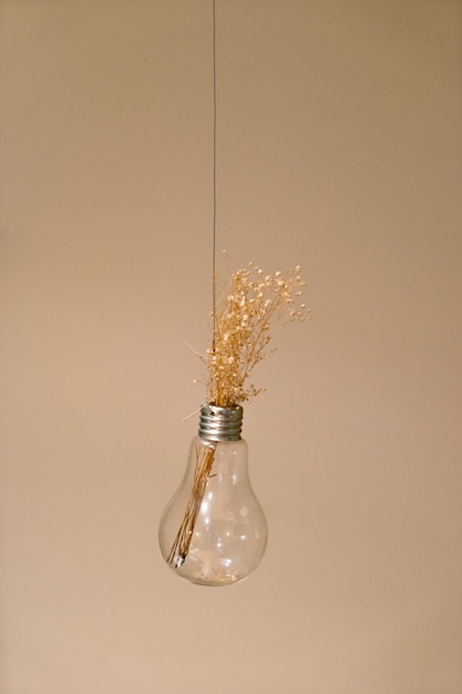 Vertical closeup shot of flower decoration in a hanging light bulb isolated on a pink background