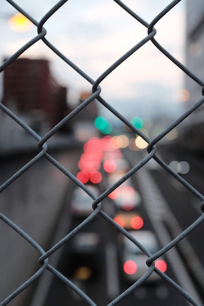 Vertical closeup shot of gray chain link fence on a blurry background of street