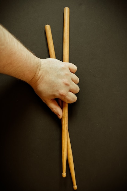Vertical closeup shot of a person's hand holding two drumsticks on a black surface