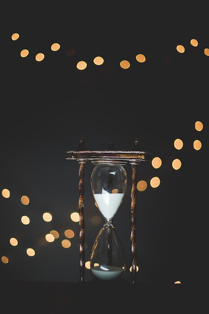 Free photo vertical closeup shot of a sand glass timer with burred lights in the background