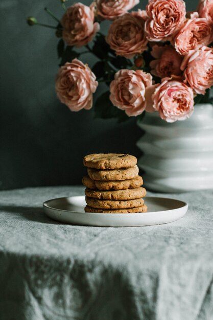 テーブルの上の花瓶にピンクのバラの近くのプレートに積み上げの焼きたてのクッキーの垂直のクローズアップショット