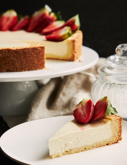 白いプレートと黒い背景の上のイチゴのチーズケーキの垂直クローズアップショット