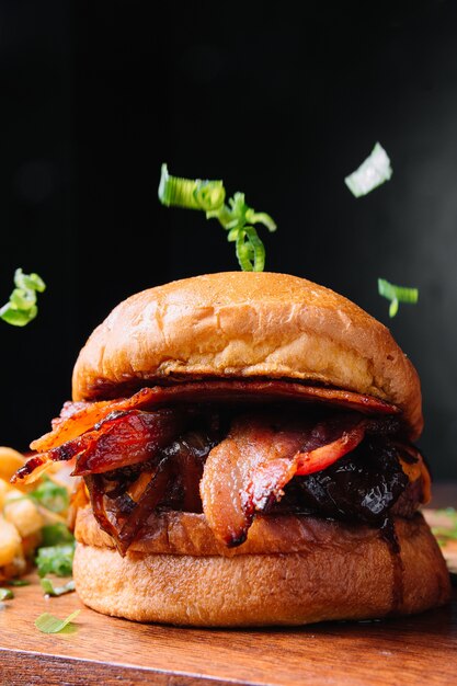 Vertical closeup shot of a tasty burger with bacon on a black wall