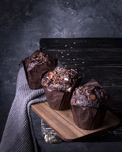 Vertical closeup shot of three delicious chocolate muffins on a dark gray background