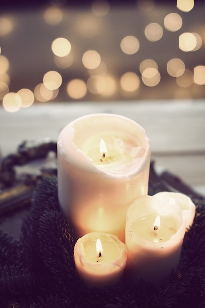 Free photo vertical closeup shot of three white burning candles with bokeh lights