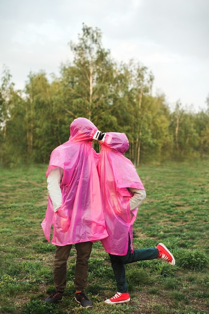 Vertical closeup shot of two people in pink plastic raincoats and VR headset kissing each other