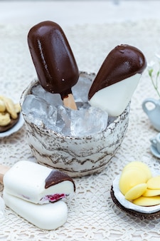 Primo piano verticale di gelato vegano su bastoncini in una ciotola con cubetti di ghiaccio su un tavolo
