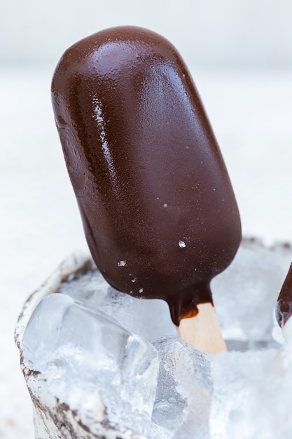 Vertical closeup shot of vegan ice-cream on sticks in a bowl with ice cubes on a table