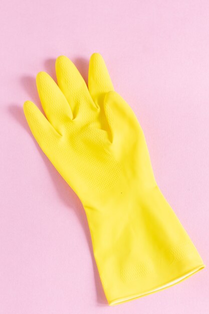 Вертикальный снимок желтой пластиковой перчатки на розовой поверхности крупным планом