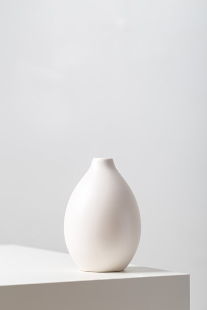 Vertical closeup of a white clay vase on the table under the lights against a white